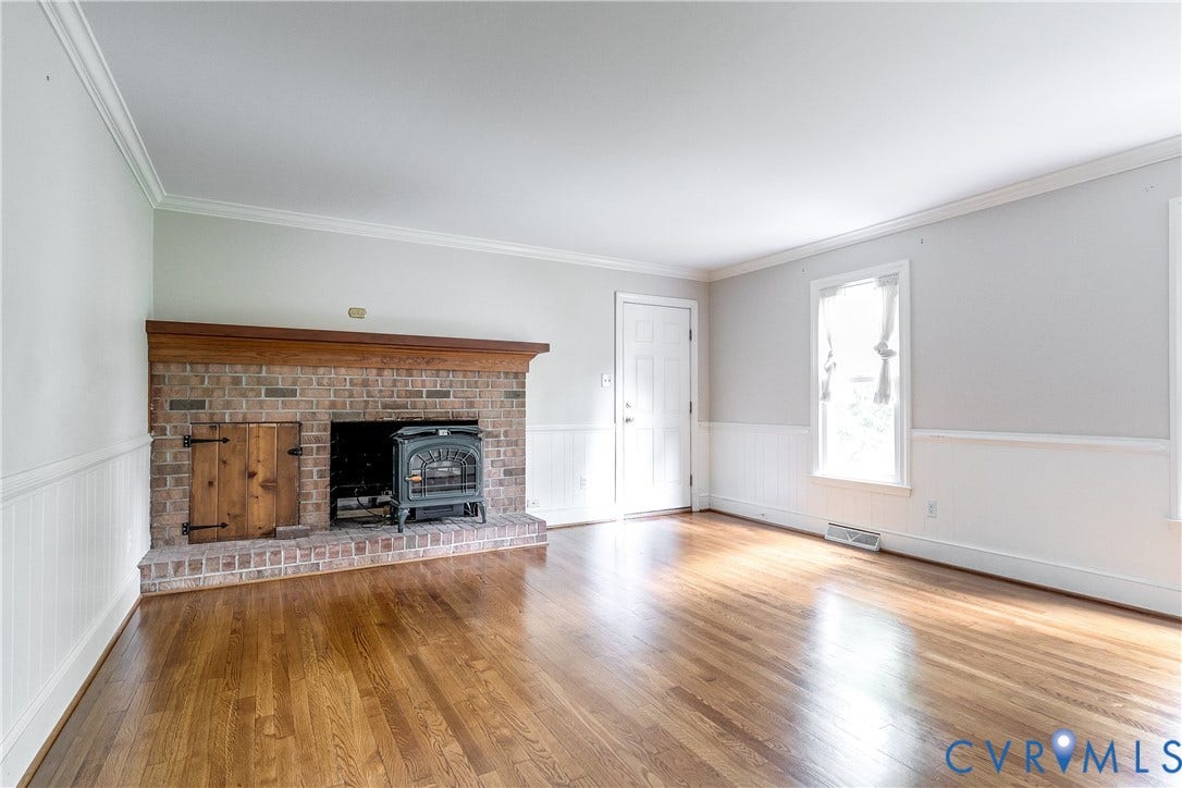3924 Belspring Road, Chester, VA 23831 Spacious room featuring a brick fireplace with a wood mantle and hearth, a dark-toned wood-burning stove, and a wood storage cubby with a paneled door