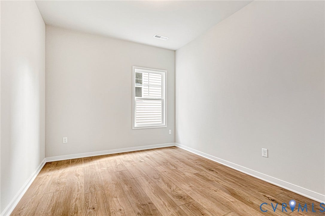 Light-filled room featuring wood-finish flooring, neutral wall paint, white trim, and a window with horizontal blinds