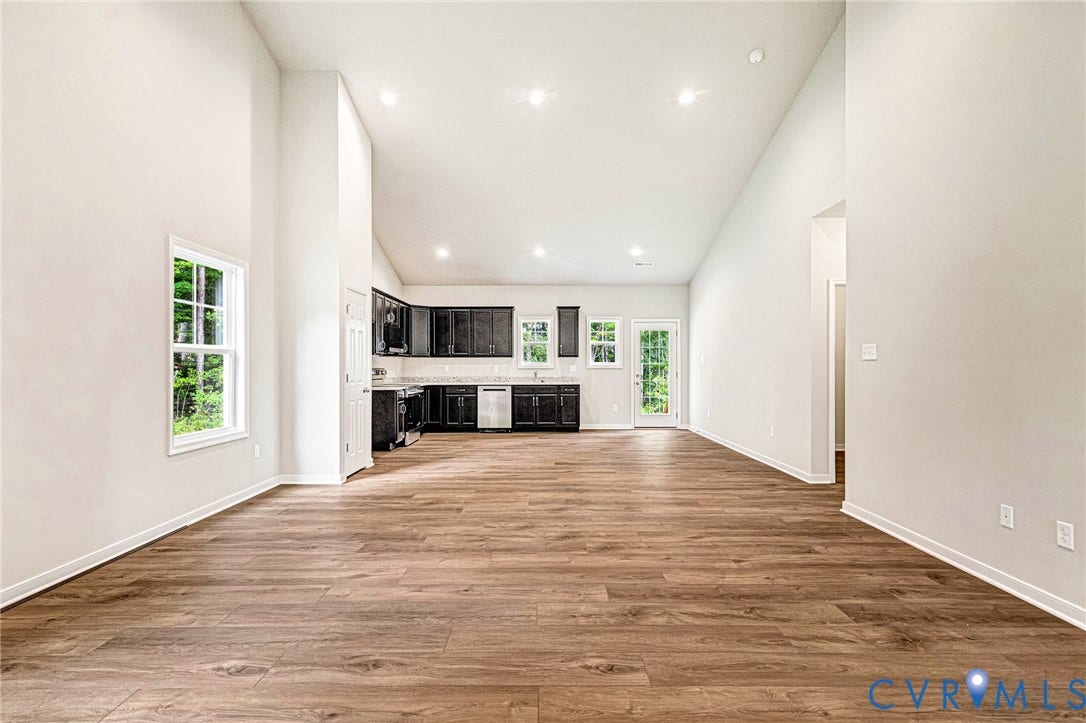 Expansive open-concept living area featuring wood-finish flooring, vaulted ceilings, and recessed lighting