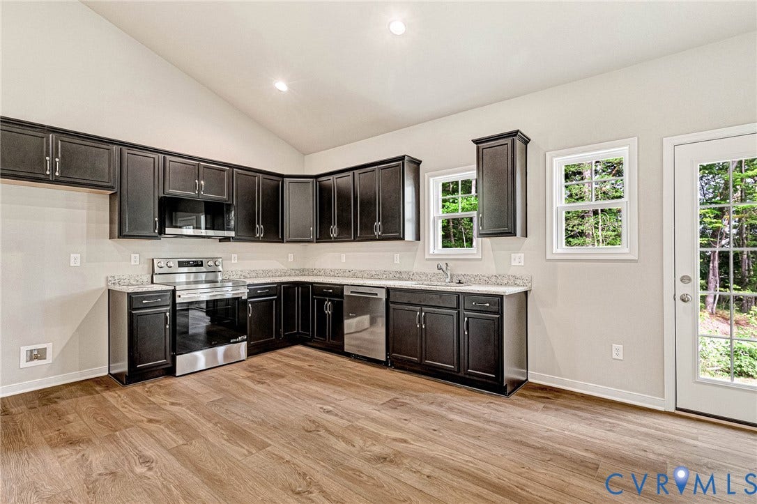 Kitchen featuring vaulted ceilings, wood-finish flooring, dark cabinetry, light countertops, and stainless steel appliances