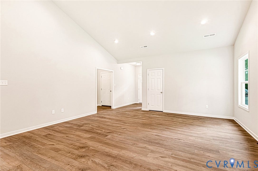 Spacious room featuring a vaulted ceiling with recessed lighting, wood-finish flooring, and white baseboards