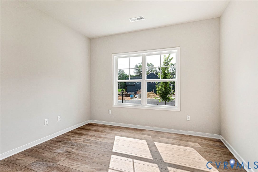 Room featuring a large white-framed window, wood-finish flooring, light neutral-toned walls, white baseboards, and a ceiling vent