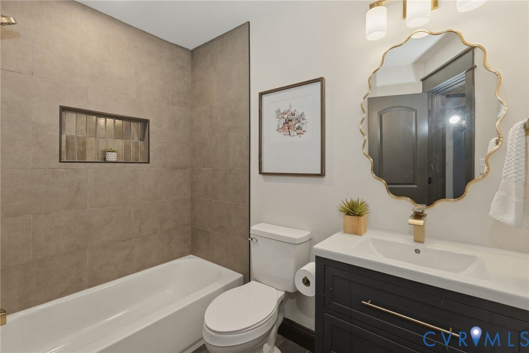 2627 Kensington Avenue, Museum District, Richmond, VA 23220 Bathroom featuring a white bathtub with gold-finish fixtures, a tiled shower surround with an integrated niche, a dark wood-finish vanity with a white countertop and basin sink, and a decorative gold-frame mirror