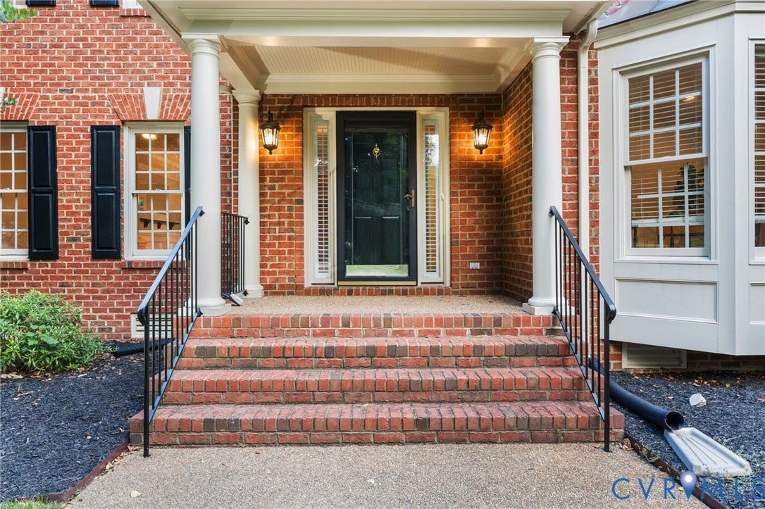 Brick facade featuring a columned portico with a dark paneled front door