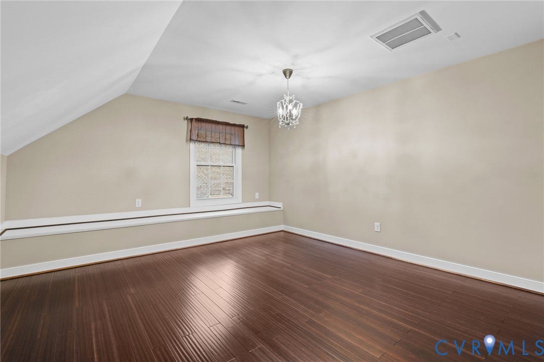 Spacious room featuring dark wood-finish flooring, a contemporary chandelier, a window with a built-in window seat, and neutral wall paint