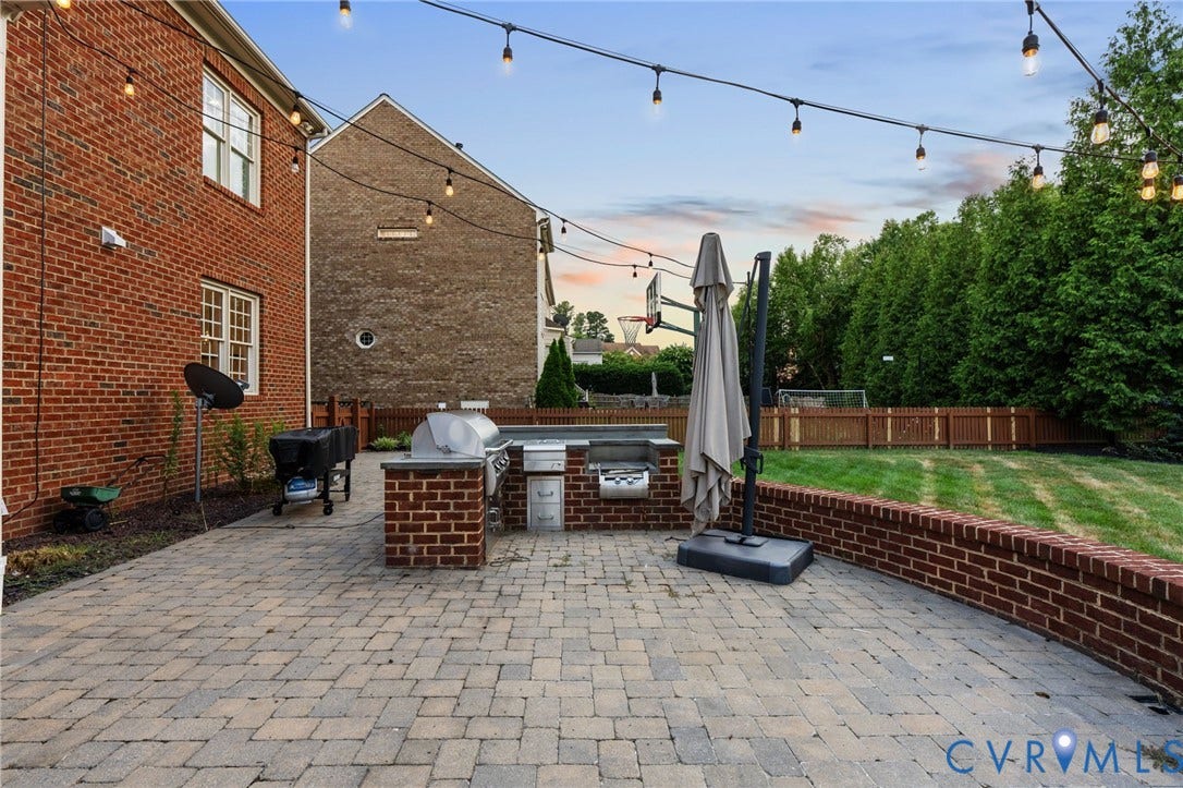 Expansive brick paver patio featuring a built-in brick and stone outdoor kitchen with grill