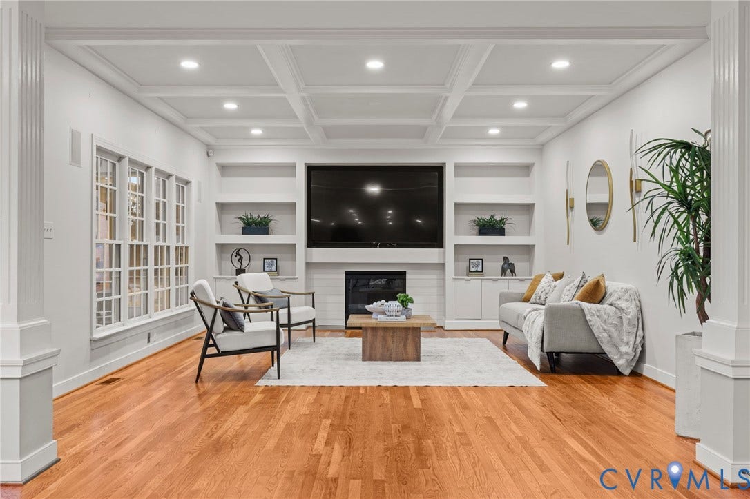 Spacious living area featuring polished wood flooring, an elegant coffered ceiling with recessed lighting, and a prominent fireplace with an integrated media center