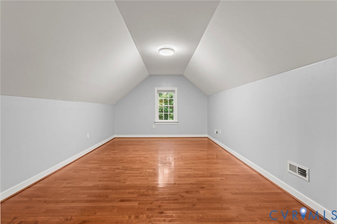Spacious room featuring sloped ceilings, a centered window, and warm wood flooring