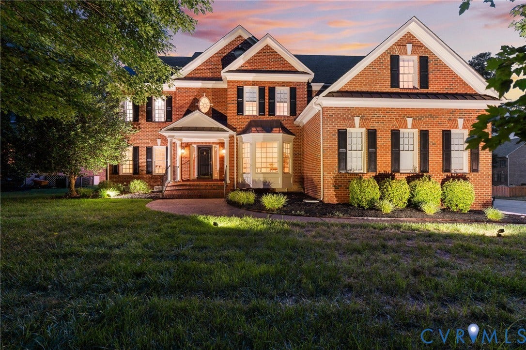 Traditional brick exterior featuring a covered portico entry, bay window, gabled rooflines, and black louvered shutters