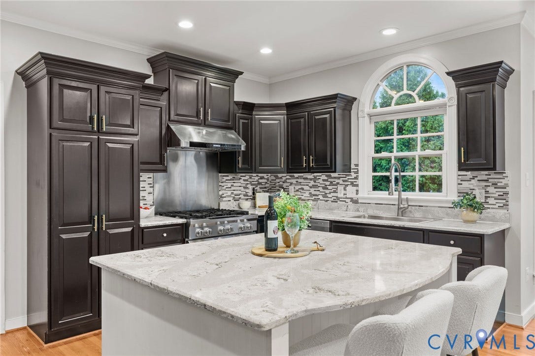 Kitchen featuring dark wood cabinetry, light-toned stone countertops, a mosaic tile backsplash, stainless steel appliances, and a window with an arched transom