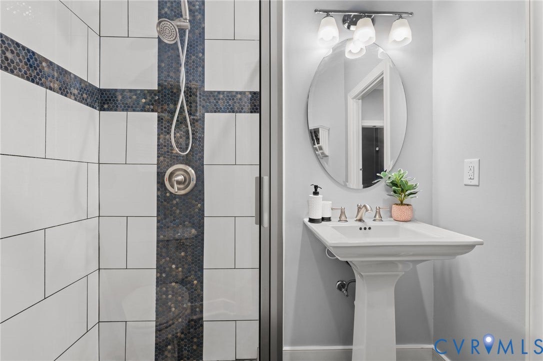 Pedestal sink with an oval mirror and a four-light vanity fixture