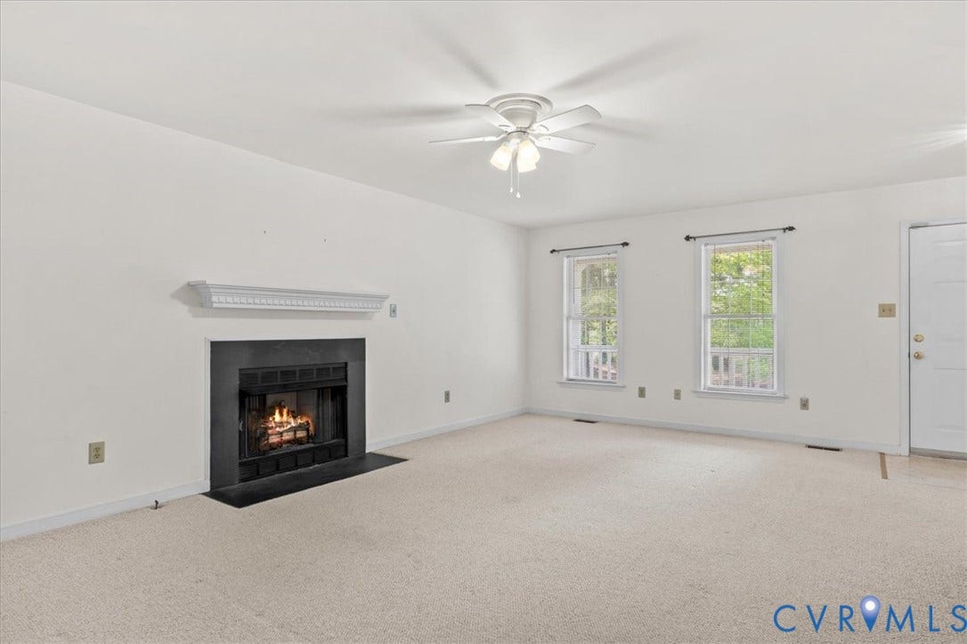2924 Warfield Ridge Terrace, Chester, VA 23831 Living area featuring a fireplace with a black surround and hearth, a decorative mantel, two windows with white trim, a ceiling fan with integrated lighting, and neutral carpeting