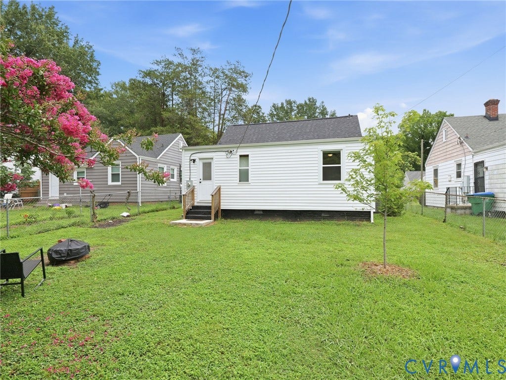 Rear exterior featuring white horizontal siding, a private entry door with wood stairs, and a newly planted tree