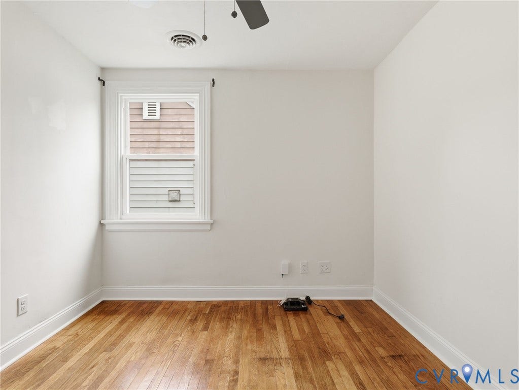 Hardwood flooring complements white walls in this room, featuring a double-hung window with white trim