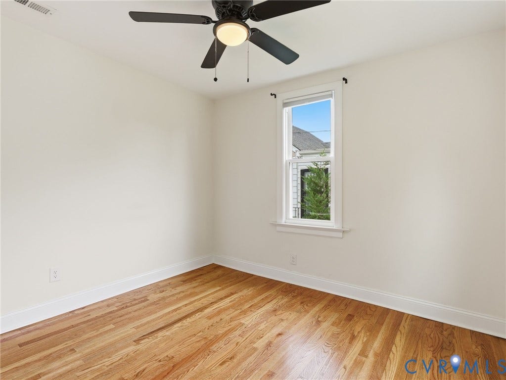 Hardwood flooring, crisp white walls, single window with white trim, black ceiling fan with integrated lighting, and white baseboards