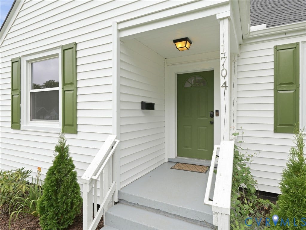 Entry features a green paneled door with an arched window, complemented by white siding and matching green shutters