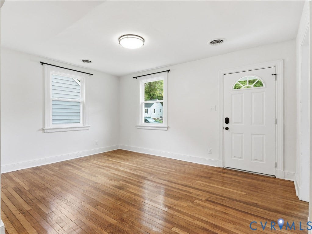 Interior room featuring wood-finish flooring, white walls, and a white paneled door with an arched window insert