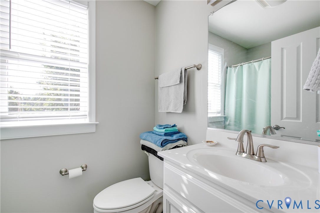 1301 Dance Street, Randolph, Richmond, VA 23220 Bathroom vanity with an integrated sink and brushed nickel faucet, a wall-mounted mirror, and a white framed window with horizontal blinds