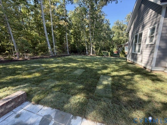 Expansive rear yard featuring new sod, mature perimeter trees, a stone patio, and a brick retaining wall