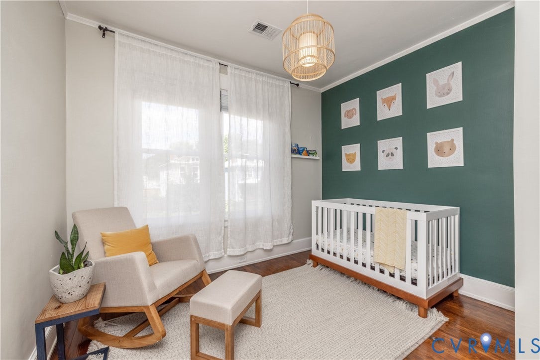 Room featuring rich wood-finish flooring, a decorative accent wall, crown molding, and two windows with sheer curtains