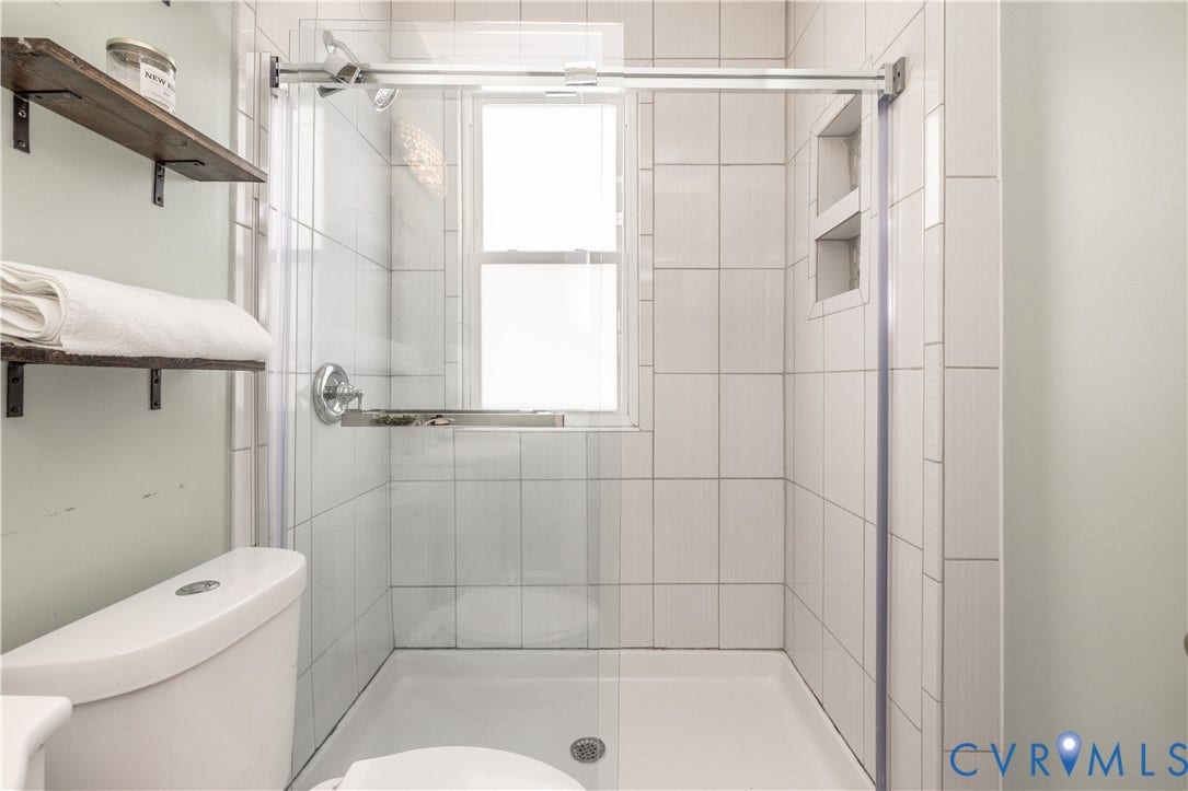 Shower enclosure featuring white subway tile, a clear glass door, and integrated shelving niches