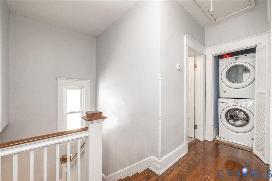 Hardwood flooring spans the upper level hallway, featuring a built-in laundry closet with a stackable washer and dryer