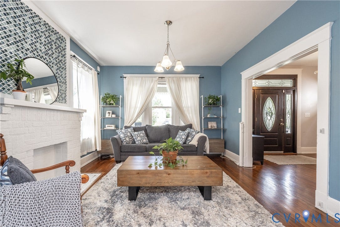Spacious living area featuring polished wood flooring and a painted brick fireplace with a decorative tile accent