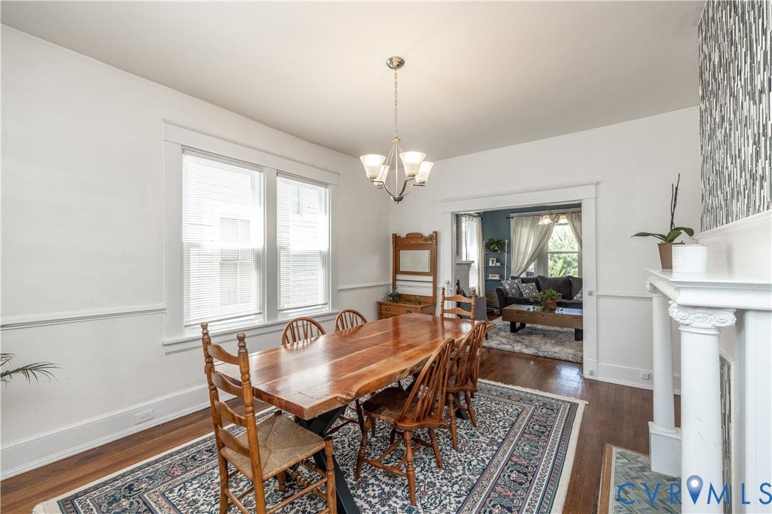 Formal dining area featuring hardwood flooring, an overhead chandelier, and a decorative fireplace with a patterned tile surround