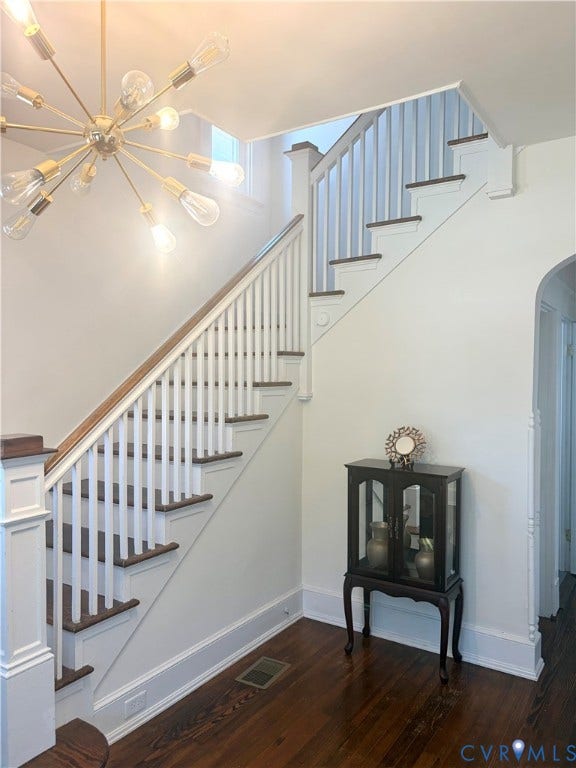 Dark wood-finish flooring, white painted risers and balusters, wood-finish handrail, and a contemporary sputnik-style chandelier