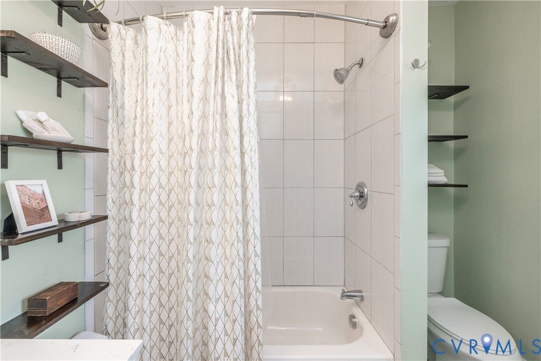 Bathroom featuring a bathtub with white subway tile surround, chrome fixtures, and light green walls