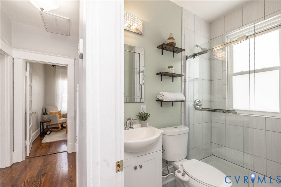 Bathroom featuring a white vanity with an integrated sink, wall-mounted mirror, and overhead sconce lighting