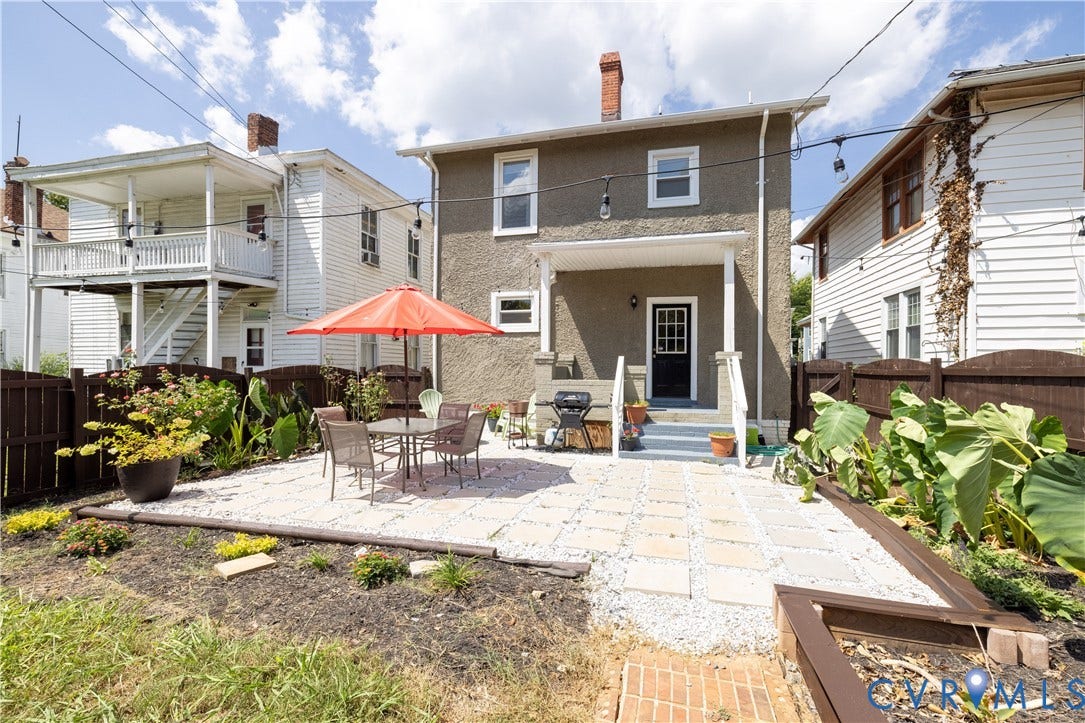 Rear exterior featuring a stucco facade, covered porch entry, and a stone paver patio