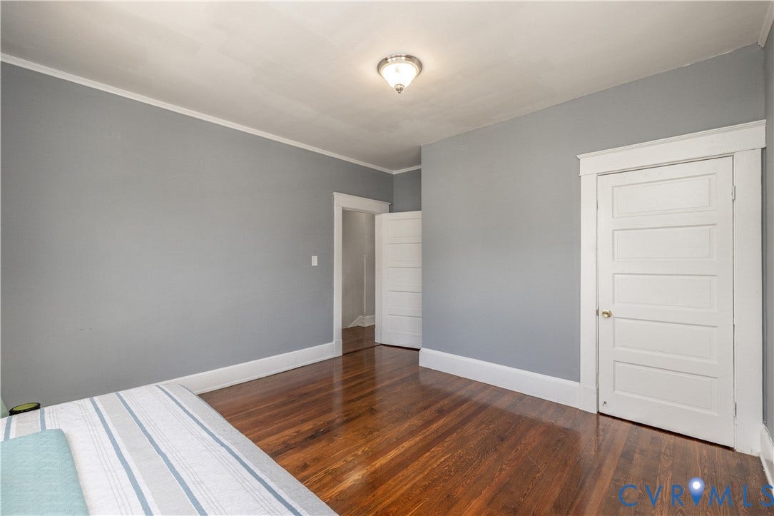 Wood-finish flooring with baseboard trim, crown molding, and a paneled interior door