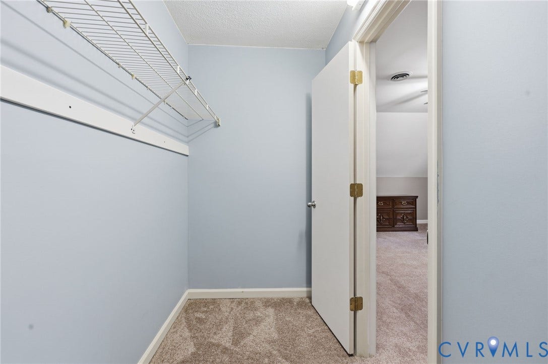 Carpeted closet space with wire shelving, light blue wall paint, and white baseboards