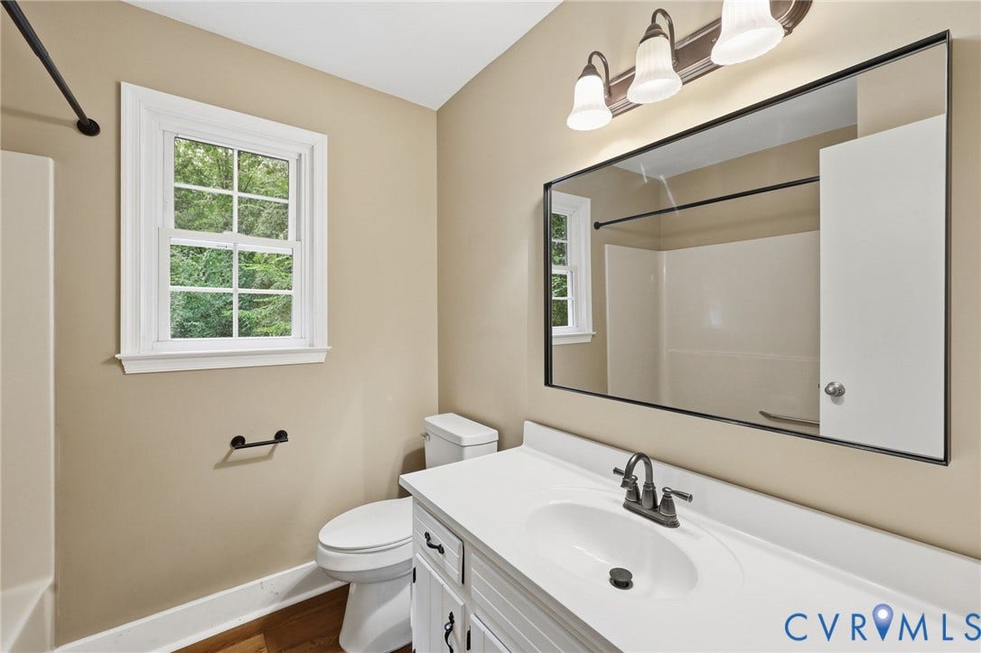 Bathroom featuring a single window, white vanity with integrated sink, rectangular mirror, and wood-finish flooring