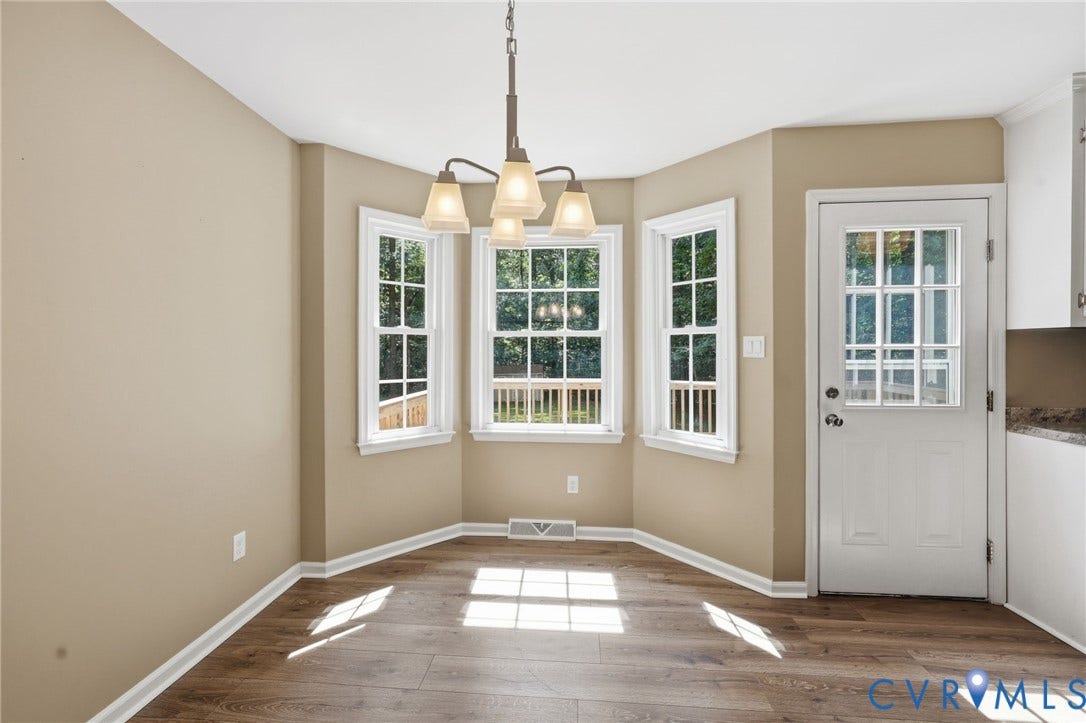 Bright dining area featuring wood-finish flooring, a contemporary chandelier, a bay window with three double-hung windows, and a panel door with a clear glass insert