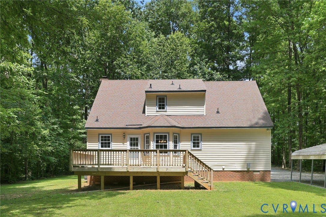 Rear exterior with a spacious wooden deck featuring stairs to the lawn, dormer windows, and light-colored siding