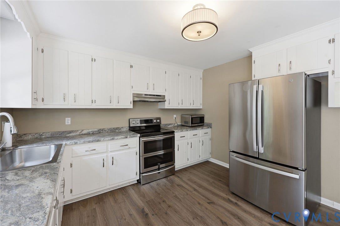 Well-appointed kitchen featuring white cabinetry, wood-finish flooring, stainless steel appliances, and stone-look countertops