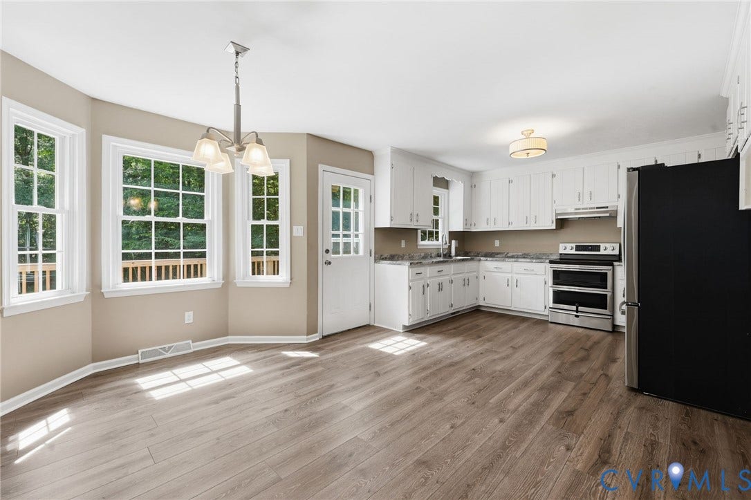 Open-concept kitchen and dining area featuring wood-finish flooring, white cabinetry, stainless steel appliances, and a dining nook with multiple windows