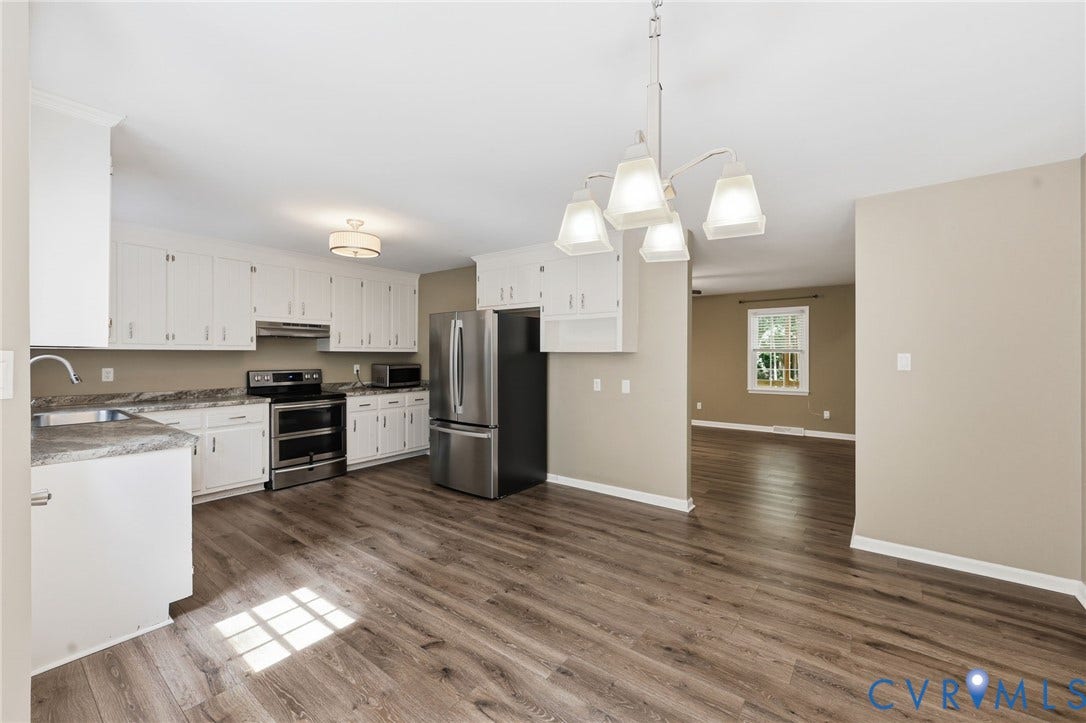 Open-concept kitchen with wood-finish flooring, white cabinetry, stainless steel appliances, and a modern chandelier