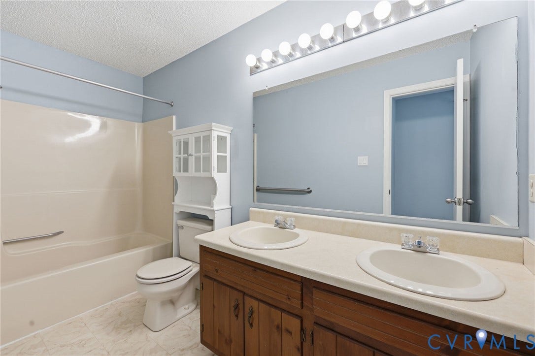 Bathroom featuring a dual-sink vanity with wood-finish cabinetry, a large vanity mirror, and a full-size bathtub with an integrated shower