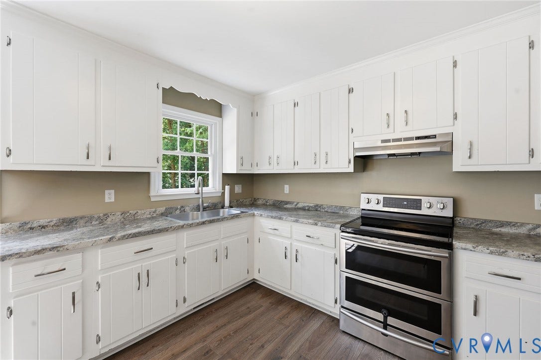 Kitchen featuring white cabinetry, grey-toned countertops, wood-finish flooring, a stainless steel double oven range, and a stainless steel sink with a window overhead