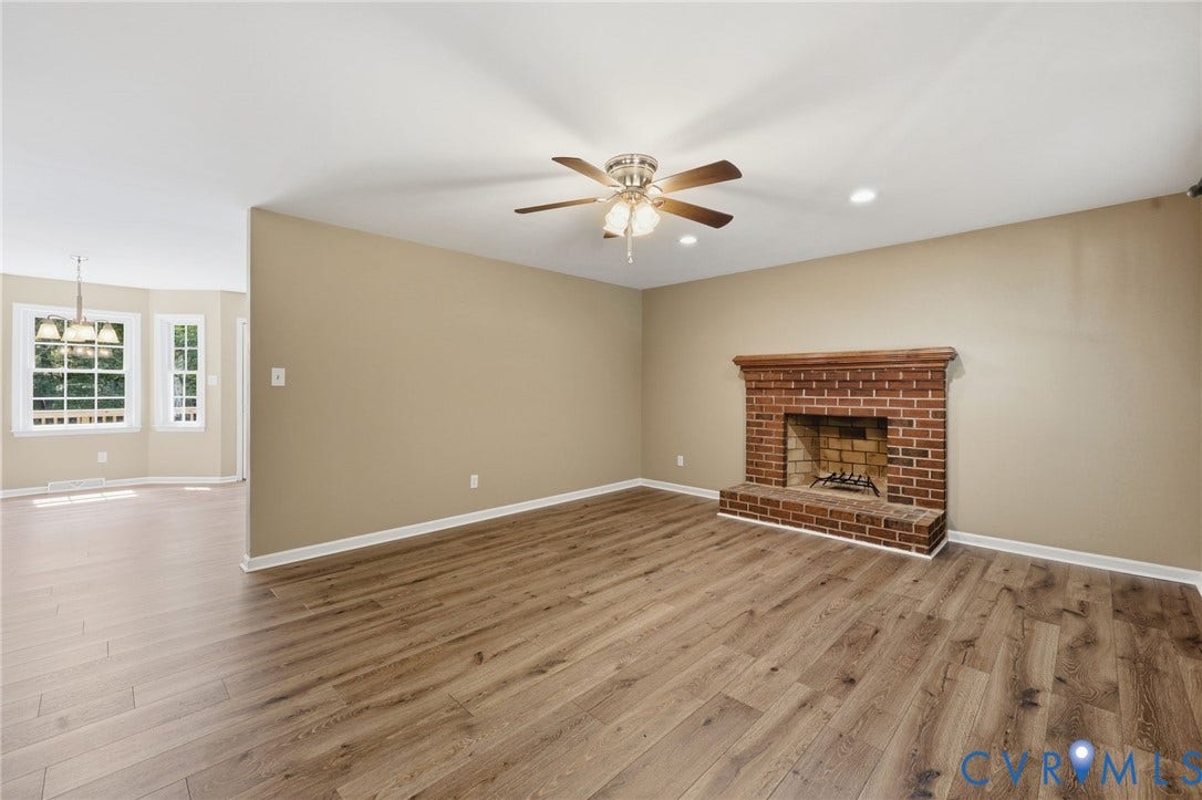 Spacious living area featuring wood-finish flooring, a brick fireplace, and a ceiling fan