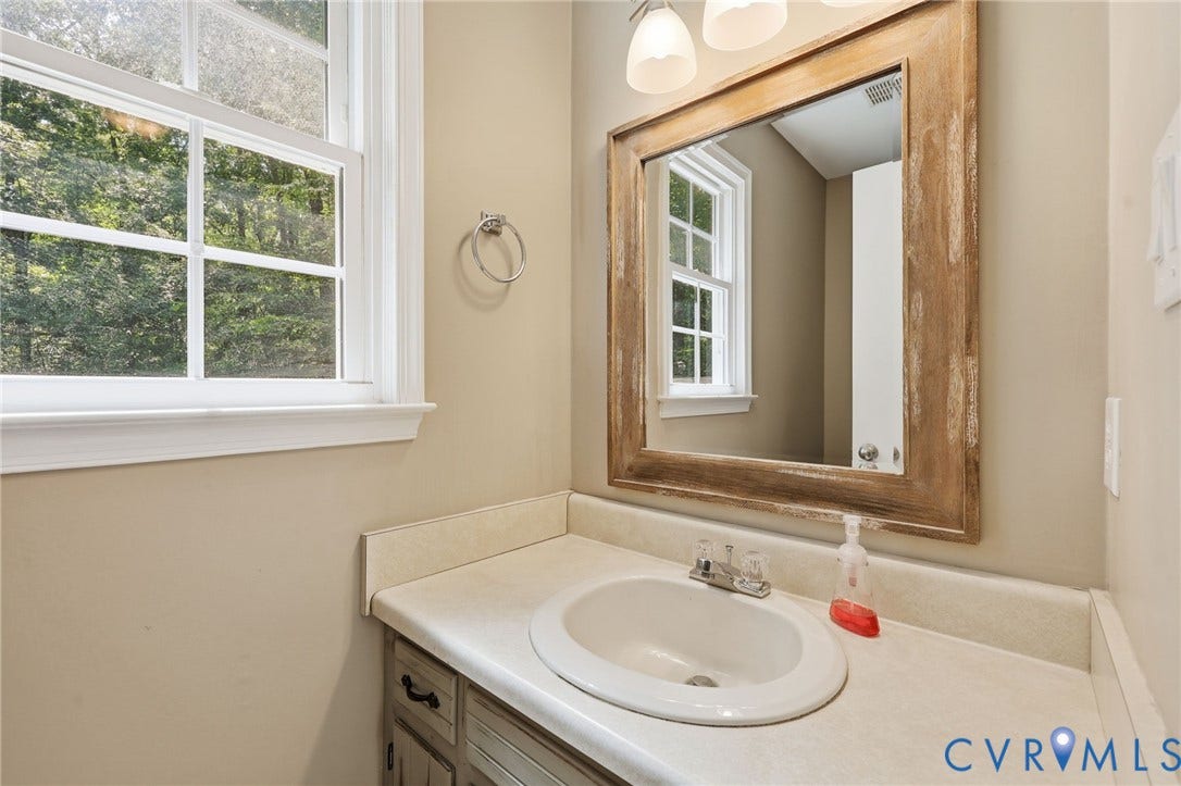 Bathroom vanity featuring a light-toned countertop, undermount sink, and a rustic wood-framed mirror