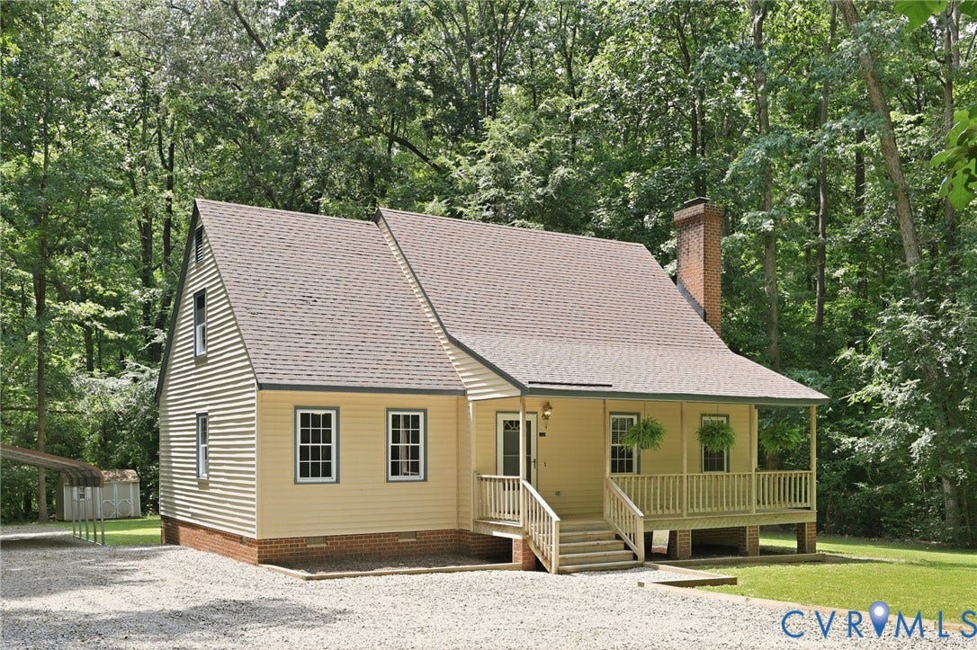 Exterior featuring light yellow siding, a covered porch with a wood railing, a brick chimney, and a gravel driveway