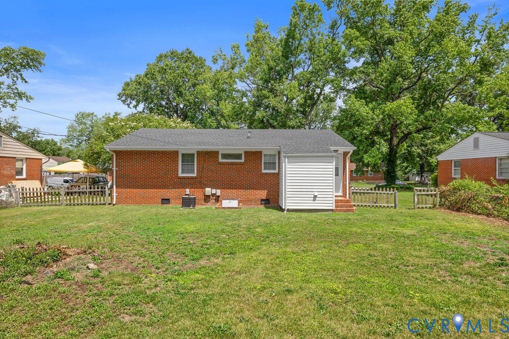 5527 Hansdale Road, Piney Knolls, Richmond, VA 23224 Expansive grassy rear yard featuring brick exterior, white vinyl siding, a dark shingle roof, and a wood picket fence