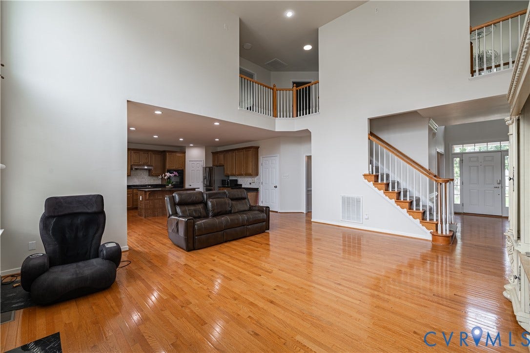 16814 Jennway Place, Moseley, VA 23120 Two-story living area featuring wood-finish flooring, a grand staircase with white balusters and wood handrails, and an open concept layout to the kitchen