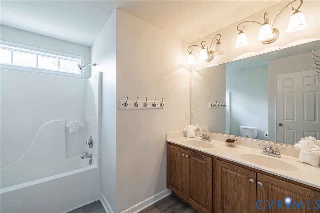 16814 Jennway Place, Moseley, VA 23120 Bathroom featuring a double vanity with wood-finish cabinetry and light-toned countertops, a large vanity mirror, and overhead sconce lighting