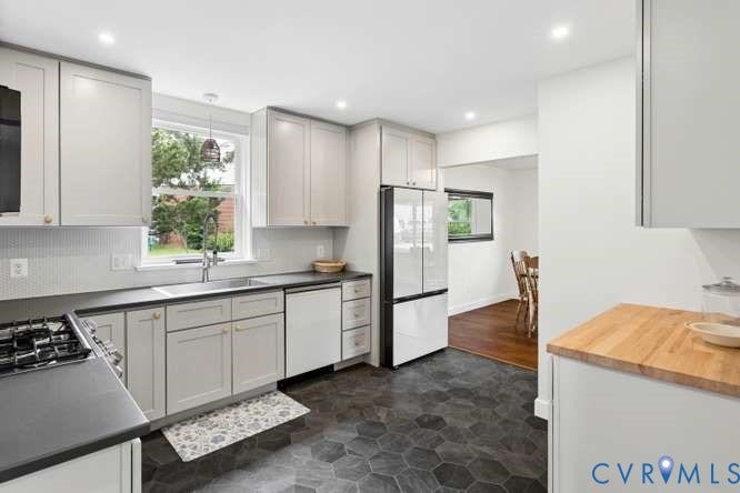 Kitchen featuring hexagon tile flooring, light gray cabinetry, dark countertops, a mosaic tile backsplash, and a built-in stainless steel sink with a window