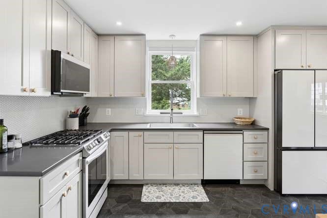 Modern kitchen featuring light cabinetry with brass hardware, dark countertops, a stainless steel gas range, and hexagonal floor tiling
